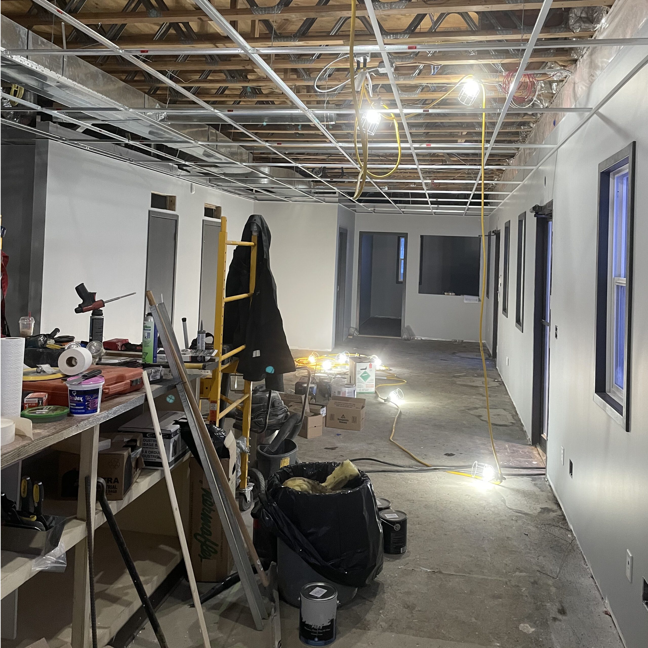 Office space under active construction with exposed ceiling, tools, wiring, and building materials