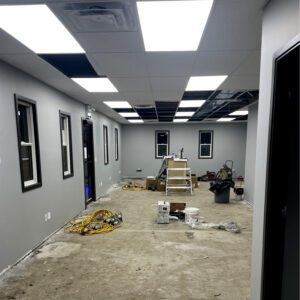 Interior office space under renovation with exposed flooring, ceiling tiles, and construction tools