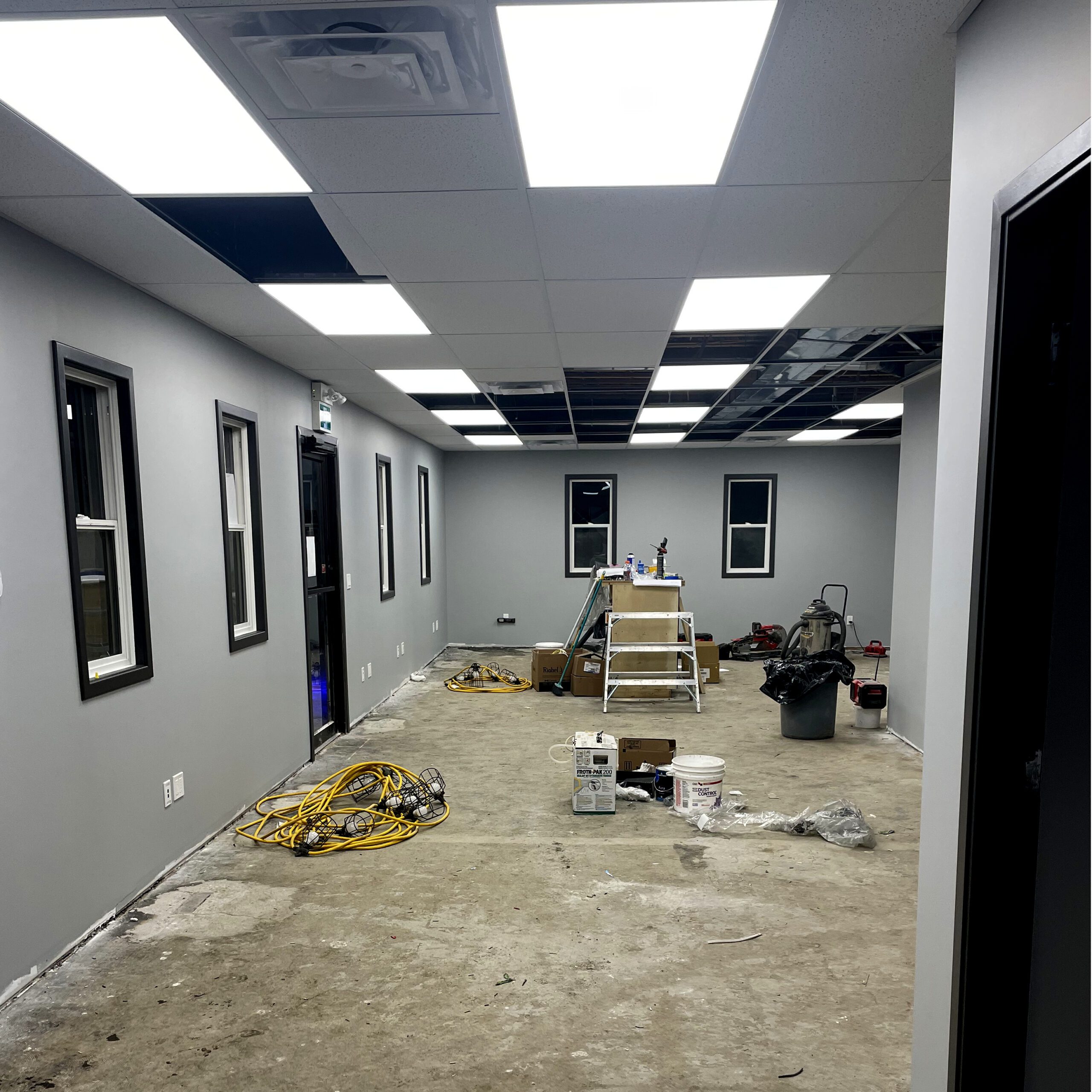 Interior office space under renovation with exposed flooring, ceiling tiles, and construction tools