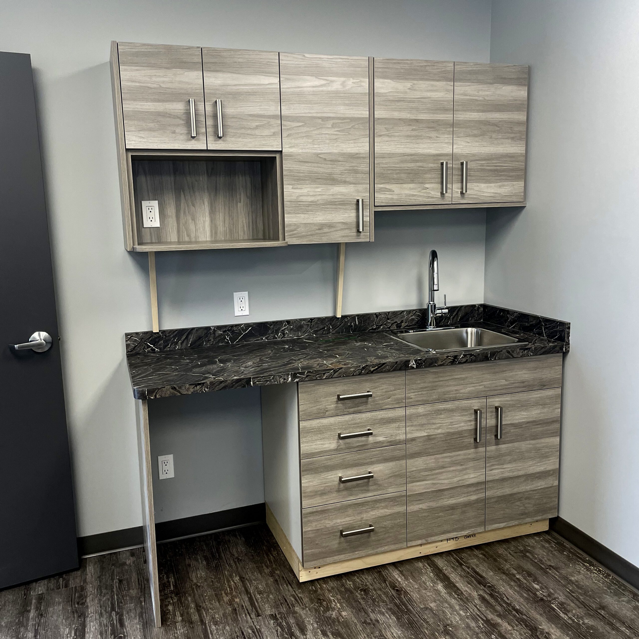 Modern kitchenette with grey wood cabinets, black marble countertop, and stainless steel sink