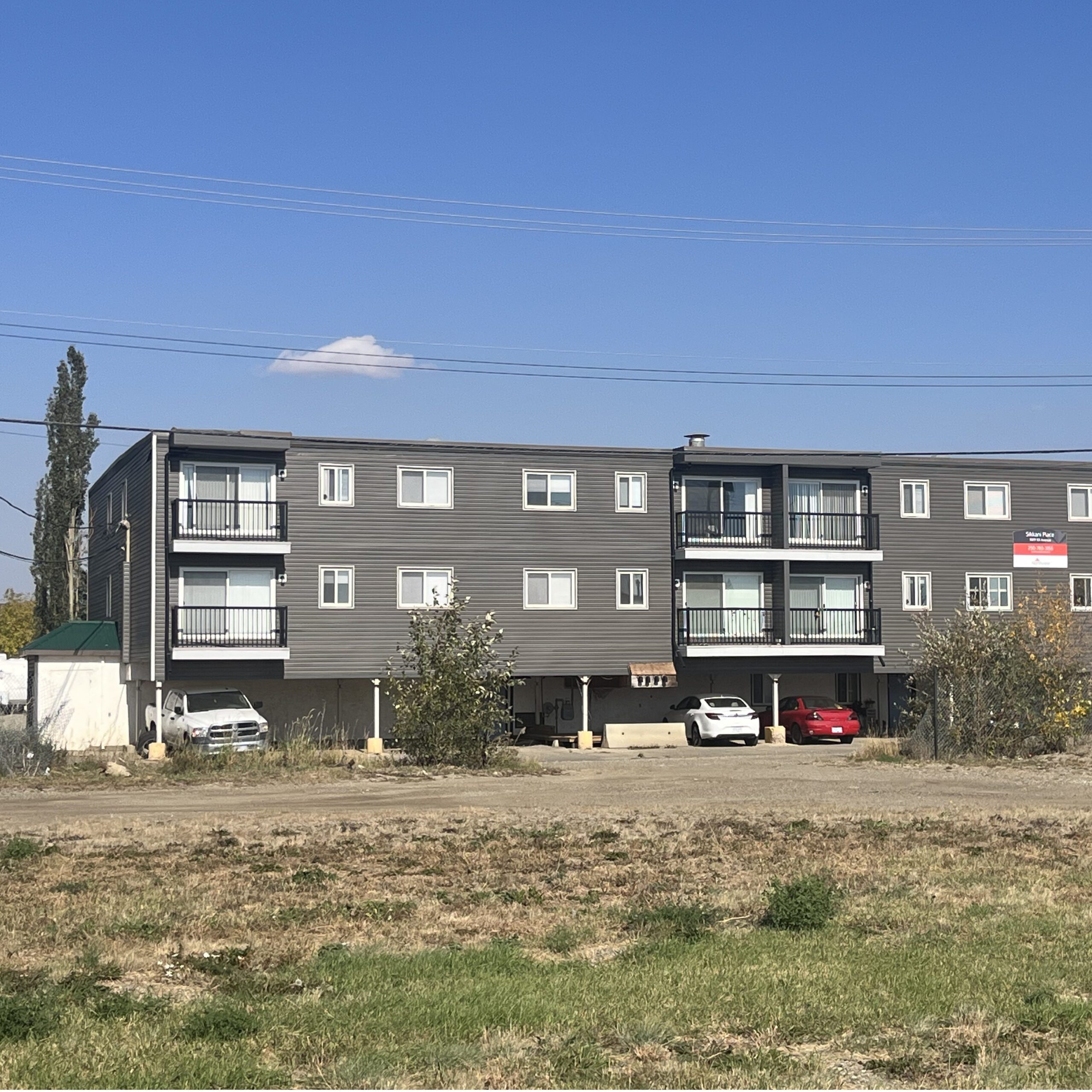 Modern three-story apartment building with balconies and parking lot in front